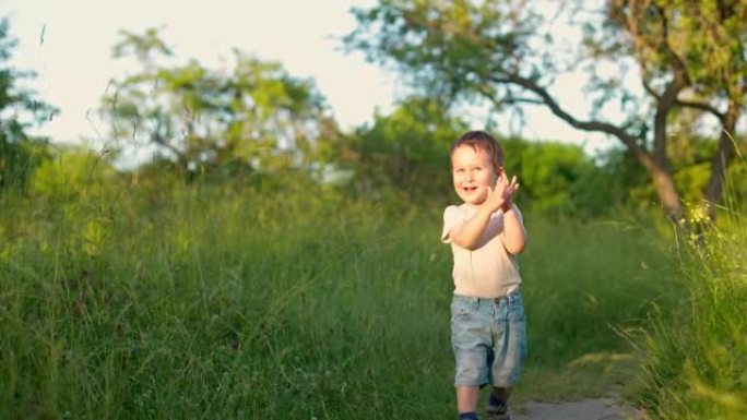 开朗可爱的男婴在绿色的花园里向前跑。快乐微笑的孩子在日落时奔跑并拍手。慢动作