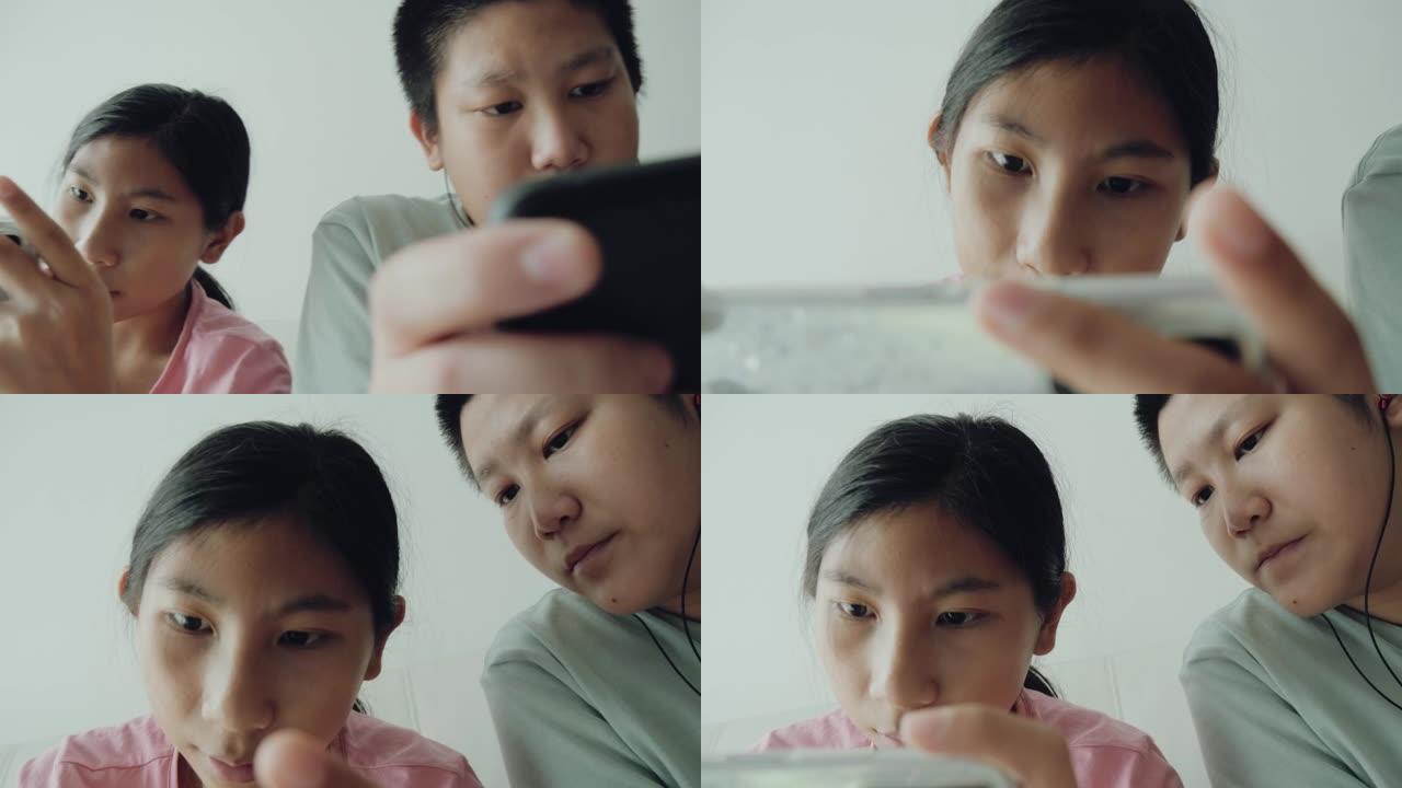 快乐的亚洲儿童在家里坐在沙发上一起在线玩手机游戏，生活方式理念。