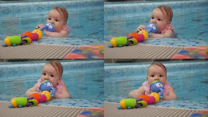一个小女孩在游泳池里拿着玩具的特写肖像，她啃着一个玩具。