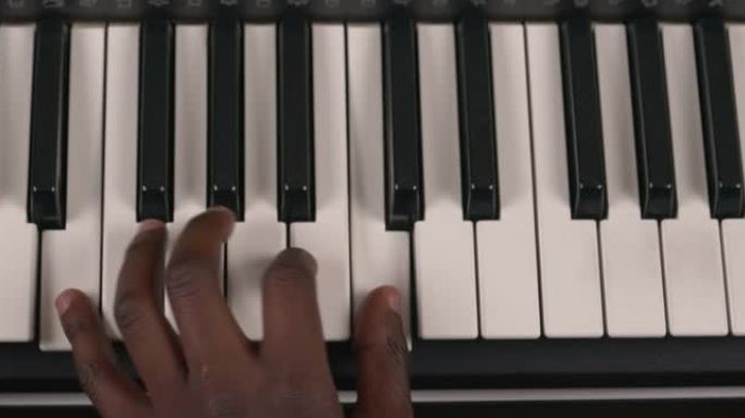非洲男性在音乐键盘上的手的俯视图。音乐家按下电子合成器上的白色键。学习弹钢琴。