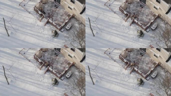 一名成年男子在冬季降雪后用铁锹从雪地上清理门廊。无人机视频正上方的鸟瞰图。