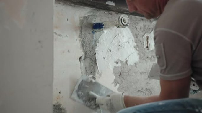 修理工用金属抹刀、抹刀和白色抹灰膏在窗下打平破旧的水泥墙，用腻子粉刷平整墙面。墙壁修复，大修概念