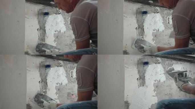 修理工用金属抹刀、抹刀和白色抹灰膏在窗下打平破旧的水泥墙，用腻子粉刷平整墙面。墙壁修复，大修概念