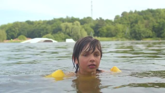 一个孩子的肖像被淹没在水中的黄色游泳漂浮物保护着。