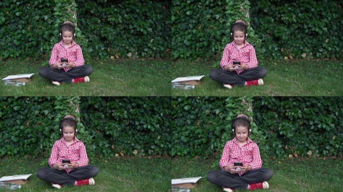 在阳光明媚的日子里，一名大学生坐在草坪上使用智能手机的肖像。高加索高中生女孩在大学公园里戴着耳机听音