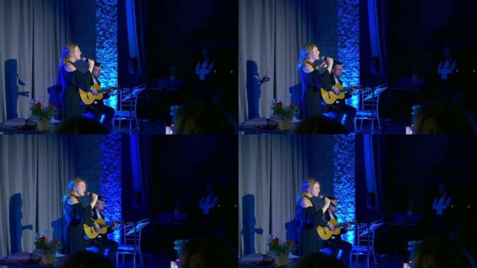 一位穿着晚礼服的年轻歌手向观众表演了一首深情的优美歌曲，而一位英俊的男人则弹吉他。平静舒适的气氛使大