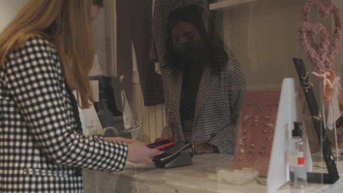 非接触式支付理念-女性客户在柜台上使用nfc技术附近的手机支付-客户端在时尚商店的终端rfid收银机