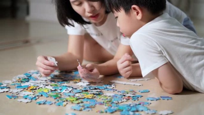亚洲家庭，母子躺在地板上做拼图游戏。女人和男孩在家里工作时发现了拼图。女人教孩子解谜。开朗的概念