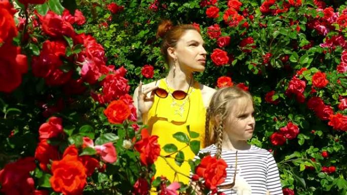 戴墨镜的女人和女孩在玫瑰背景下在花园里摆姿势