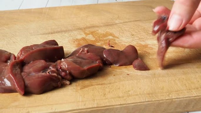 生鸡肝厨师在木菜板上用刀切成碎片。特写