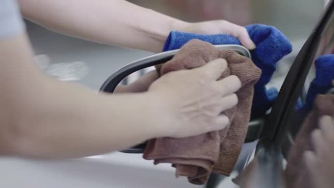 汽车抛光工人用超细纤维毛巾擦拭后视镜。