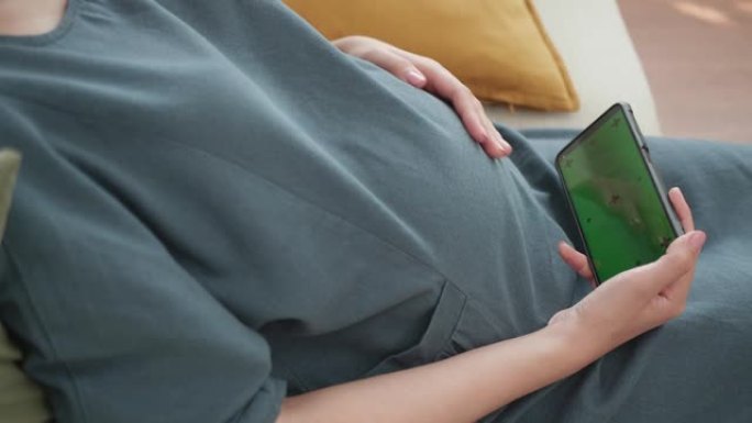 年轻孕妇手拿手机看绿屏显示器