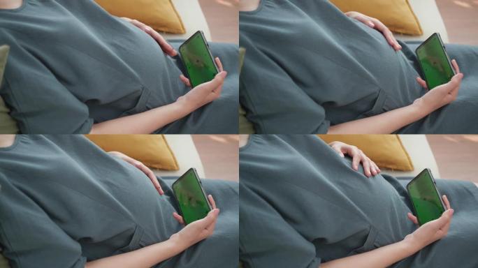 年轻孕妇手拿手机看绿屏显示器