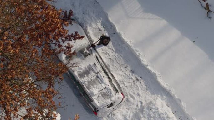 一名成年男子在冬季暴风雪后从雪地上清洗汽车。无人机视频正上方的鸟瞰图。