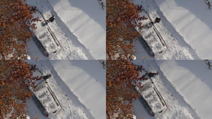 一名成年男子在冬季暴风雪后从雪地上清洗汽车。无人机视频正上方的鸟瞰图。