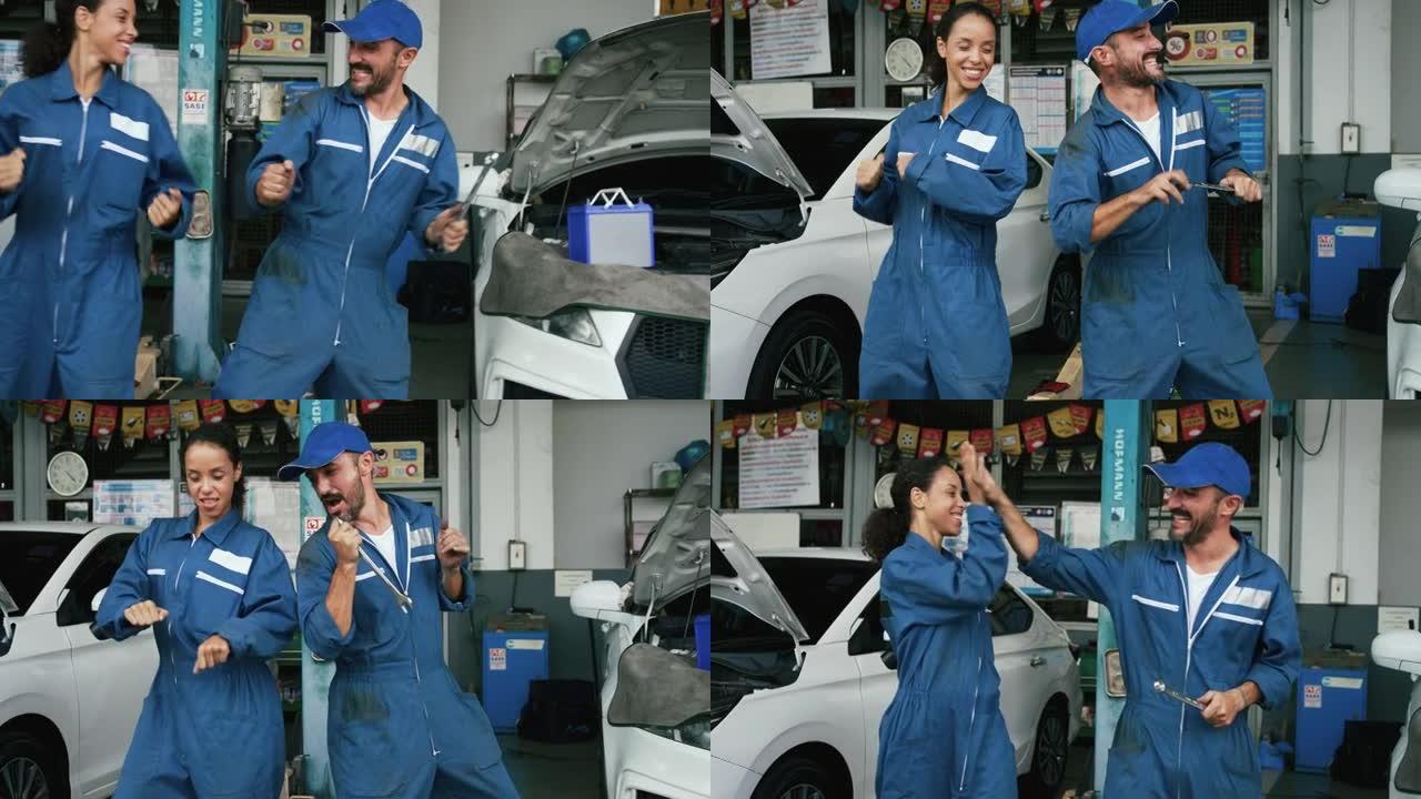 积极的机械师男女在修理厂跳舞。快乐自信的服务肖像人们在室内工作场所玩得开心。