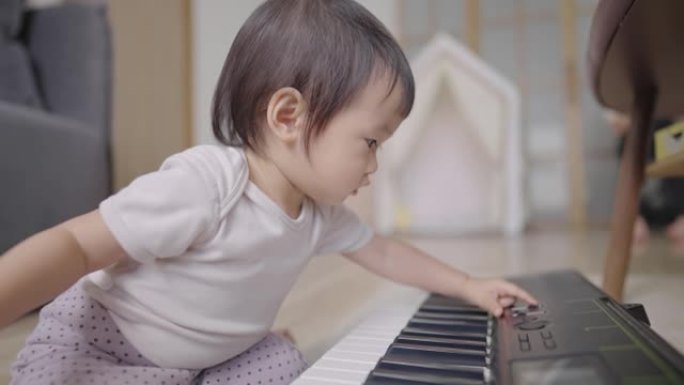 一个可爱的亚洲婴儿好奇地检查每个电子钢琴按钮的不同声音，一个顽皮的聪明的女婴坐在地板上，家里有教育乐