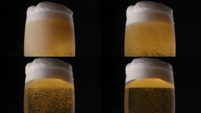 黑色背景上的一杯淡啤酒。气泡和泡沫慢慢爬到啤酒杯的顶部。顺时针旋转。