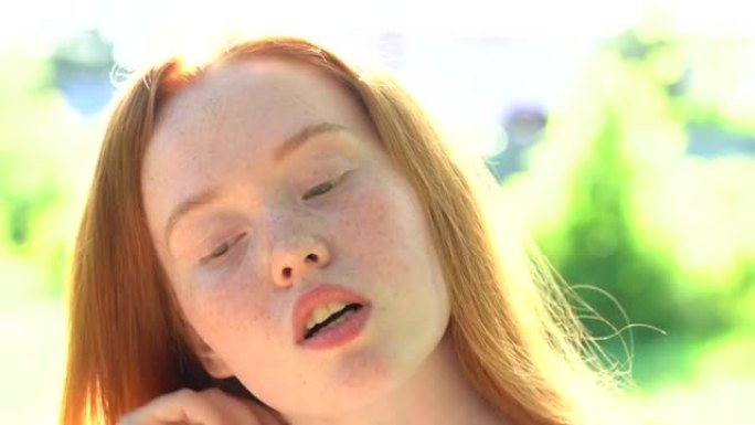 肖像一个微笑的年轻女子，红头发和雀斑在明亮的阳光草地的背景下。