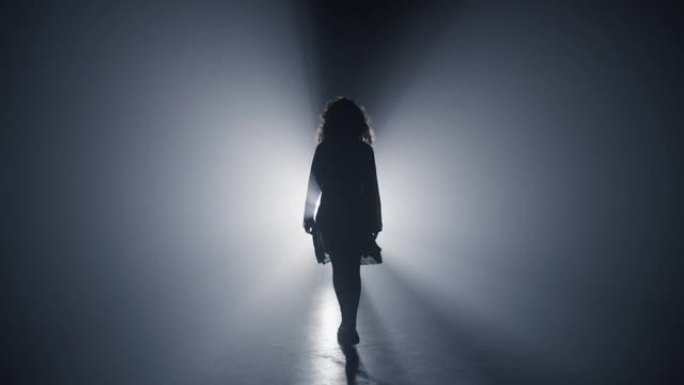 走着黑暗的剪影女孩。女人直奔相机的黑暗背景