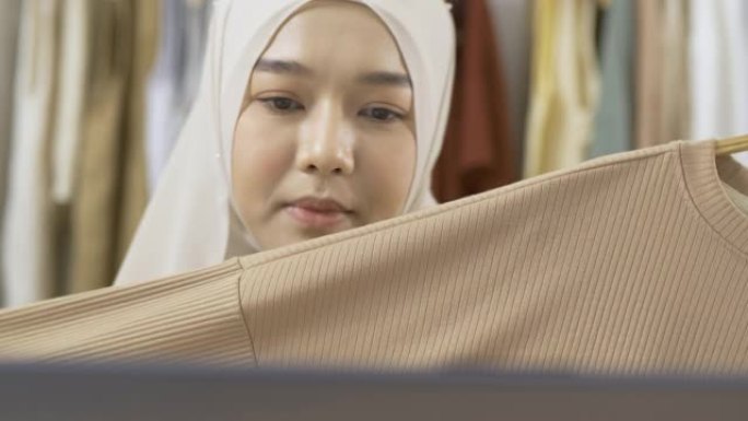 年轻美丽的亚洲女人正在她的服装店直播。她与顾客交谈并解释她的产品。