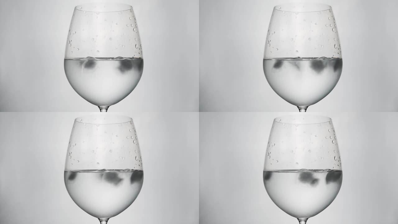 特写清澈的水在生动的玻璃葡萄酒与白色背景和照明在工作室与冰块旋转运动显示清凉的水饮料和透明溢出的冷冻