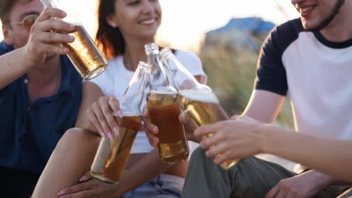 一群朋友在日落时以慢动作在海边享受着举杯、喝啤酒、放松的乐趣。年轻的男人，女人喜欢在温暖的夏日晚会上