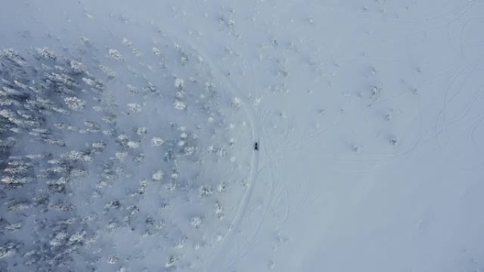 在瑞典寒冷的冬季森林中，一辆雪地摩托车在雪地上拍摄的俯视图无人机。