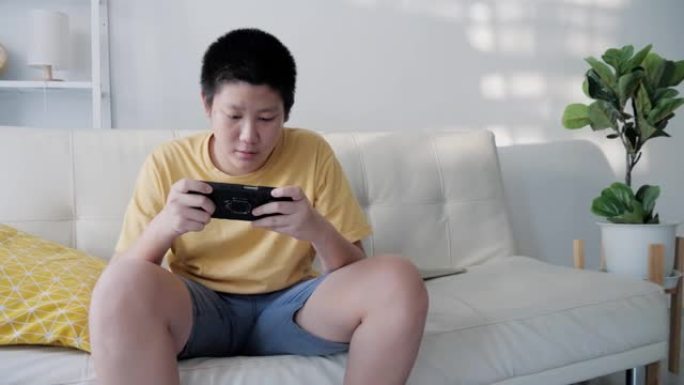 亚洲男孩在家沙发上玩在线手机游戏，生活方式概念。