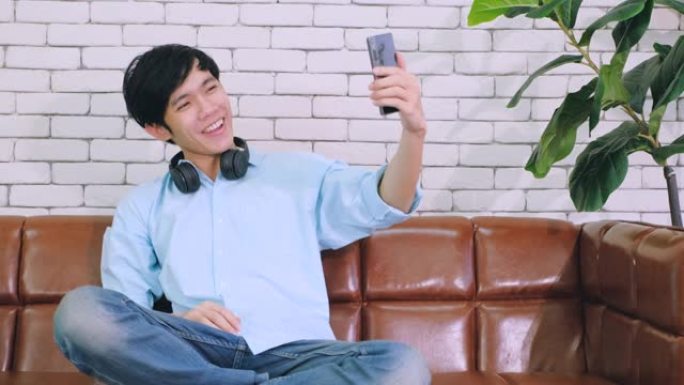 年轻的亚洲男子在手机上给远方的朋友打视频，并在家庭办公室用手挥手打招呼