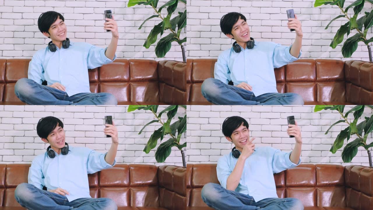 年轻的亚洲男子在手机上给远方的朋友打视频，并在家庭办公室用手挥手打招呼