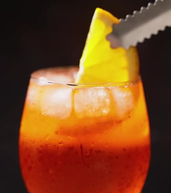 酒保在鸡尾酒里放一片橙子。黑色背景上的鸡尾酒喷喷。一杯夏季橙色鸡尾酒。垂直屏幕方向，9:16