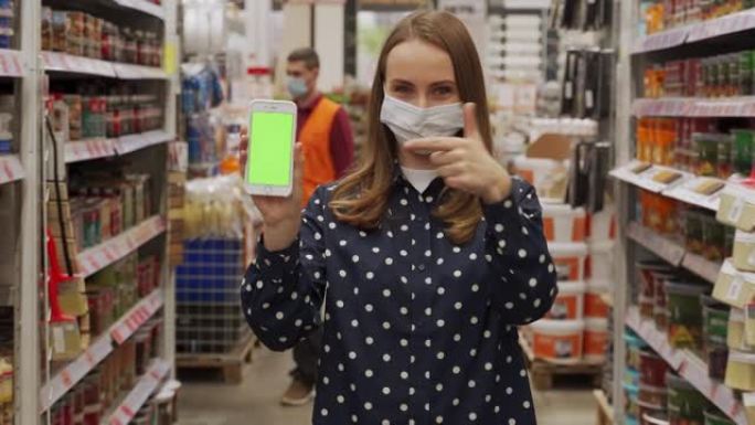 戴着防护口罩的女人，指着智能手机的绿色屏幕，看着五金店的相机