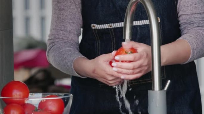 一名妇女用水龙头在水流下洗成熟的西红柿