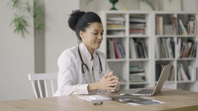 一位年轻的女医生与患者进行在线视频咨询，并检查肺部快照。美国黑人妇女坐在医院办公室的桌子旁。特写。慢