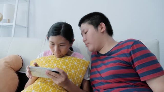 快乐的亚洲男孩和他的妹妹一起在家里坐在沙发上玩网络游戏，生活方式理念。