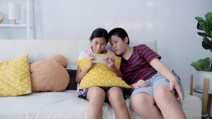 快乐的亚洲男孩和他的妹妹一起在家里坐在沙发上玩网络游戏，生活方式理念。