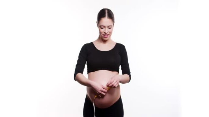 怀孕的白人年轻女子的美丽身体使用卷尺检查白色工作室背景下的婴儿发育，医疗保健和健康。健康腹部健康怀孕