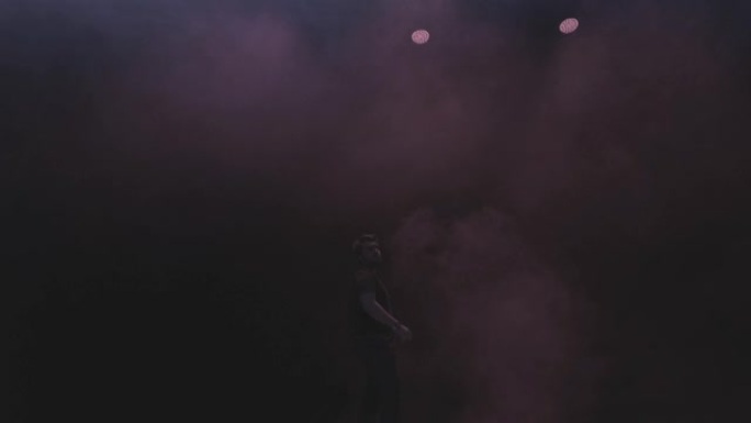 一名歌手年轻人的表演出现在黑暗背景下的蒸汽烟雾中