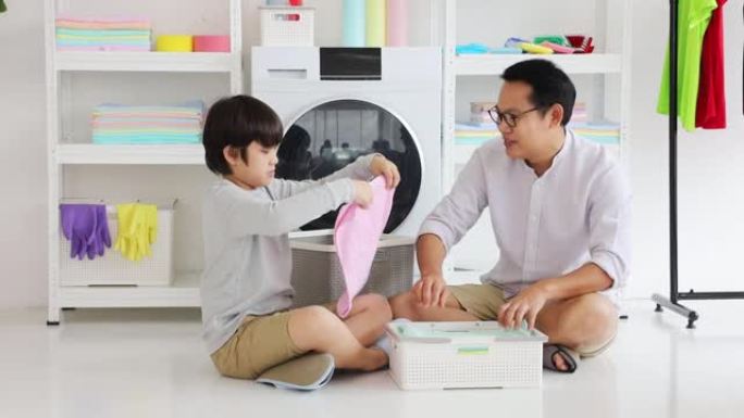 亚洲父子俩互相帮助，一起洗衣服后将衣服叠好，做日常琐事