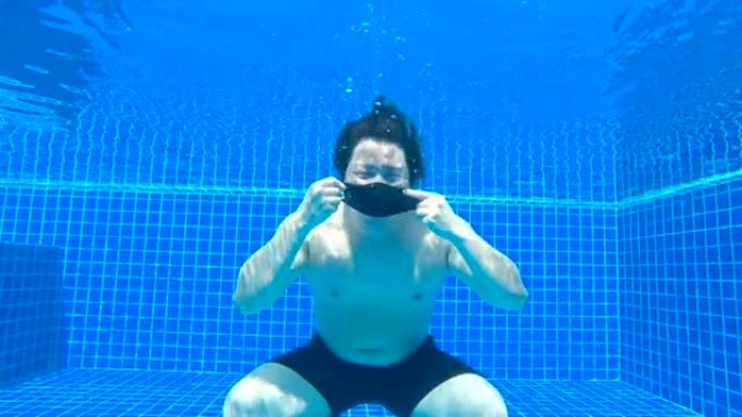 新型冠状病毒肺炎日冕病毒大流行期间，亚洲男子戴着黑色面罩，在游泳池水下竖起大拇指。