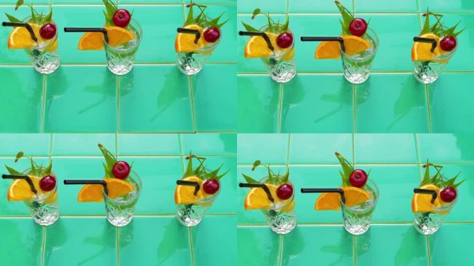 清爽的夏季饮料在水晶眼镜，叶子樱桃橙色在绿色瓷砖背景。甜冷天然鸡尾酒炎热的夏日。苏打水水果浆果薄荷滋