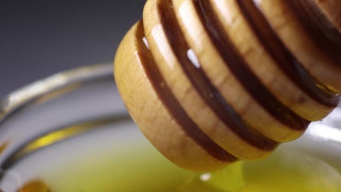 新鲜的金色蜂蜜从木制蜜勺中倒出精美