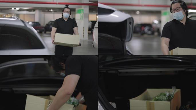 亚洲男子拿着纸盒和农产品走向汽车。