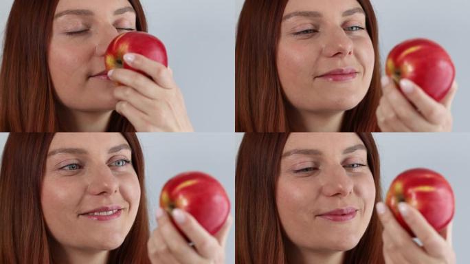 快乐的年轻女子手里拿着新鲜成熟的红苹果，闻到孤立在灰色背景上的有机水果。健康饮食。