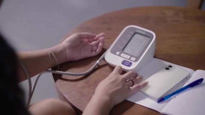年轻的亚洲妇女正在家里用数字压力表自己检查血压和心率。