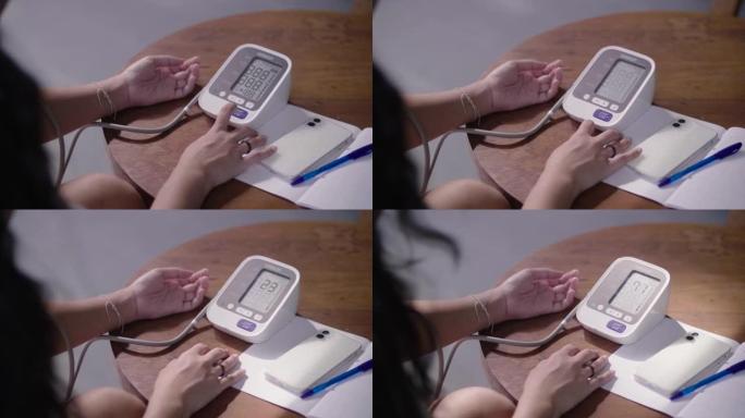 年轻的亚洲妇女正在家里用数字压力表自己检查血压和心率。