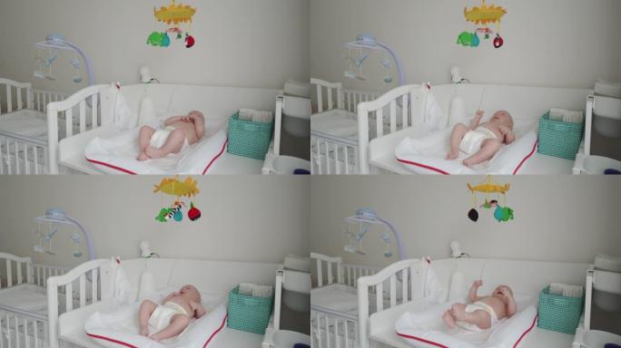 可爱的3个月大的婴儿在白色换衣桌上看着玩具手机