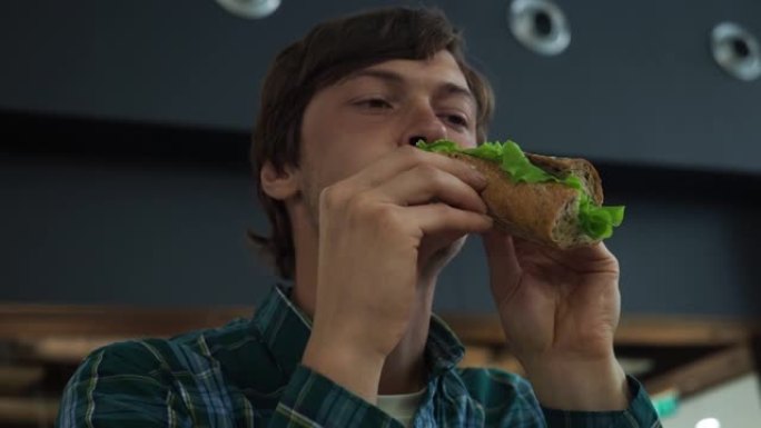 成年白人饥饿的男性在商场餐厅吃三明治。特写