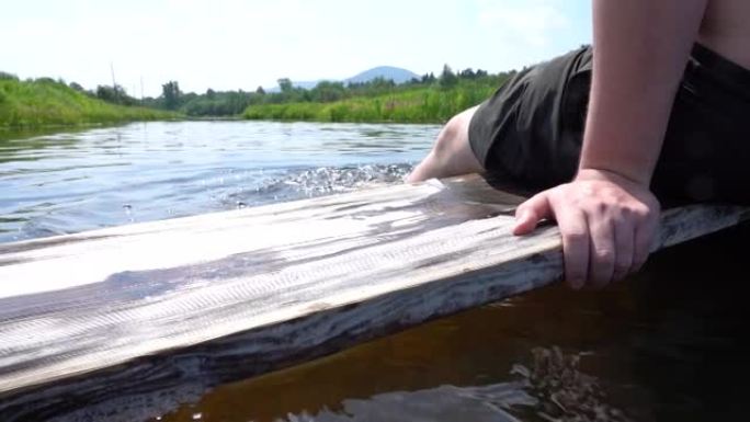 一个男人坐在一块木板上，把他的脚放在河里，享受着他的暑假
